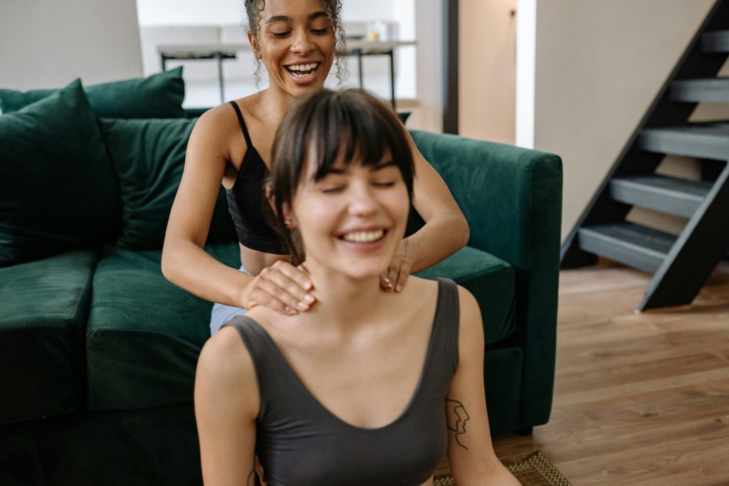 Two women enjoy a relaxing neck massage at home, highlighting friendship and wellness.